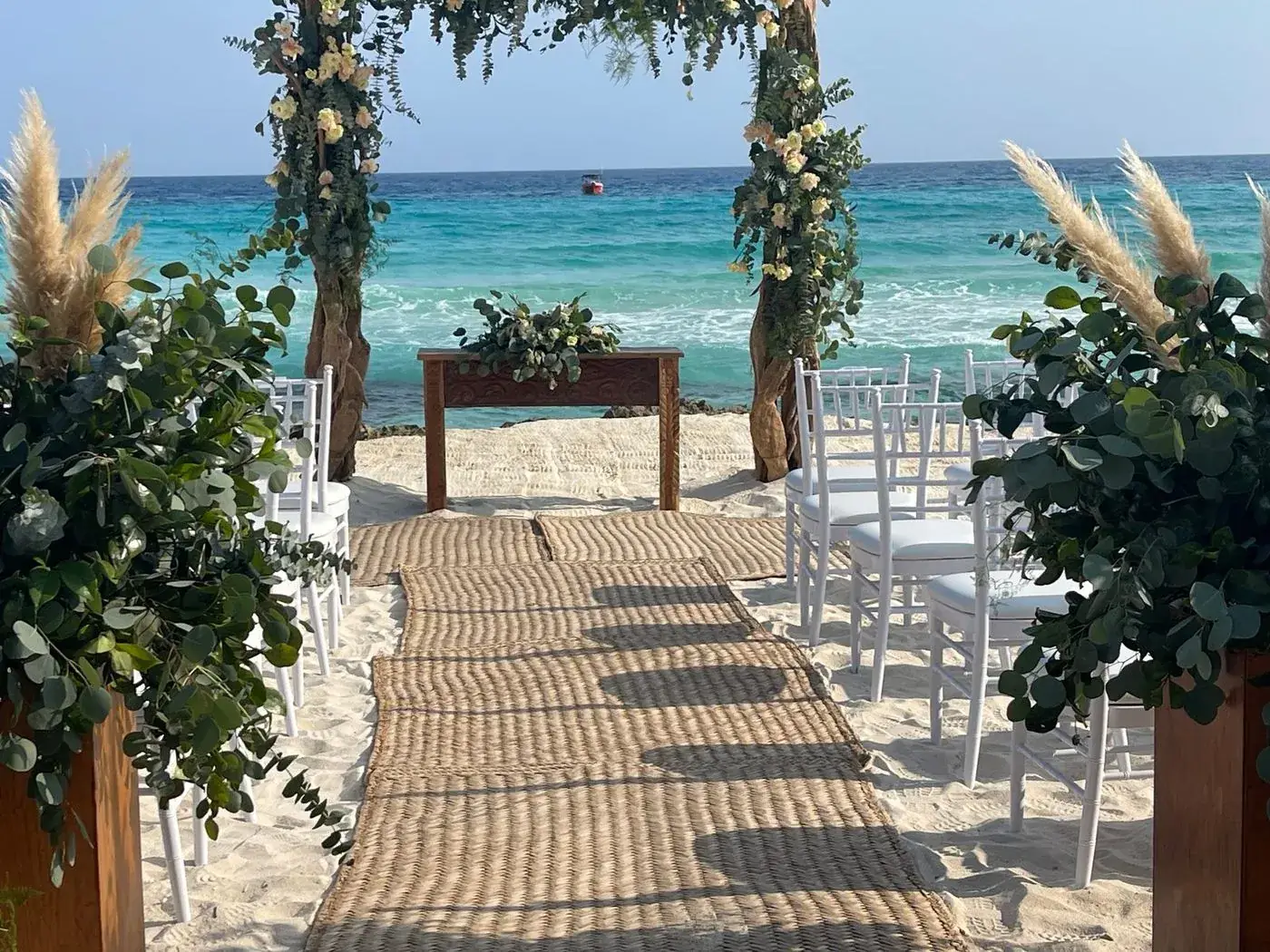 Caribbean beach wedding aisle with driftwood floral arch, pampas grass, and turquoise ocean backdrop