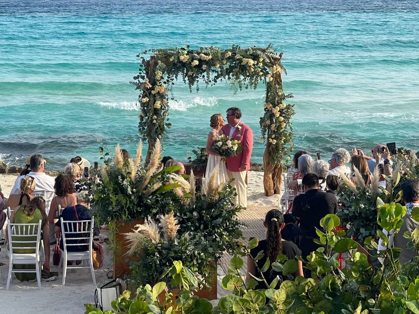 Bride and groom exchanging vows under a floral driftwood arch on a Caribbean beach at a destination wedding