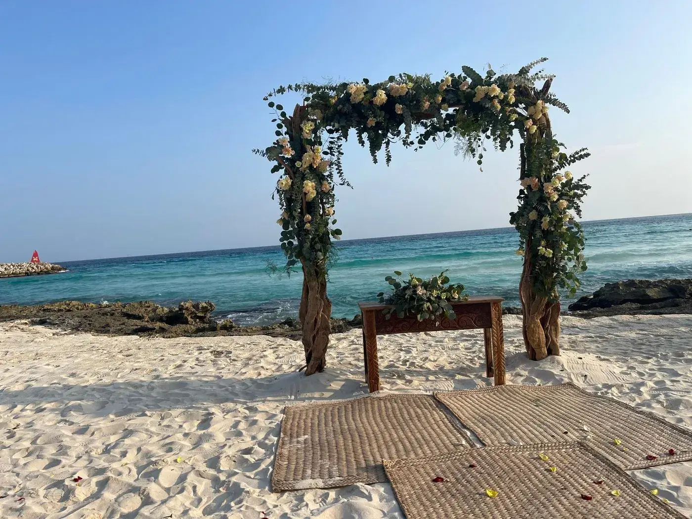 Driftwood and eucalyptus wedding arch on white sand beach overlooking turquoise Caribbean water