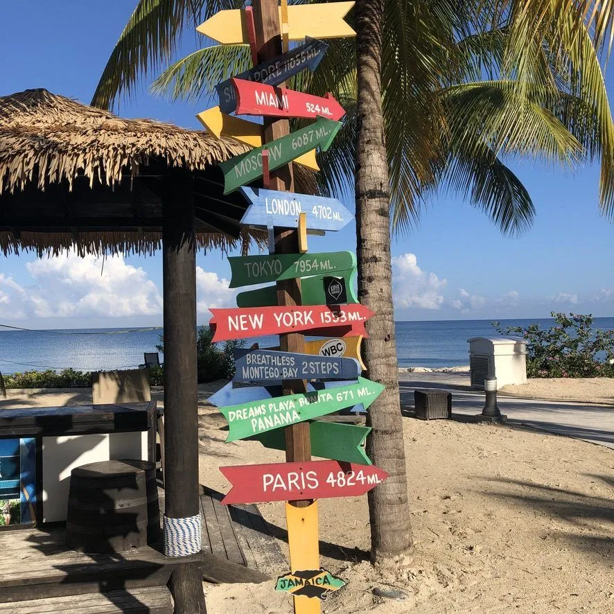 Colorful directional signpost on a Jamaican Caribbean beach pointing to Miami, London, Tokyo, New York and Paris
