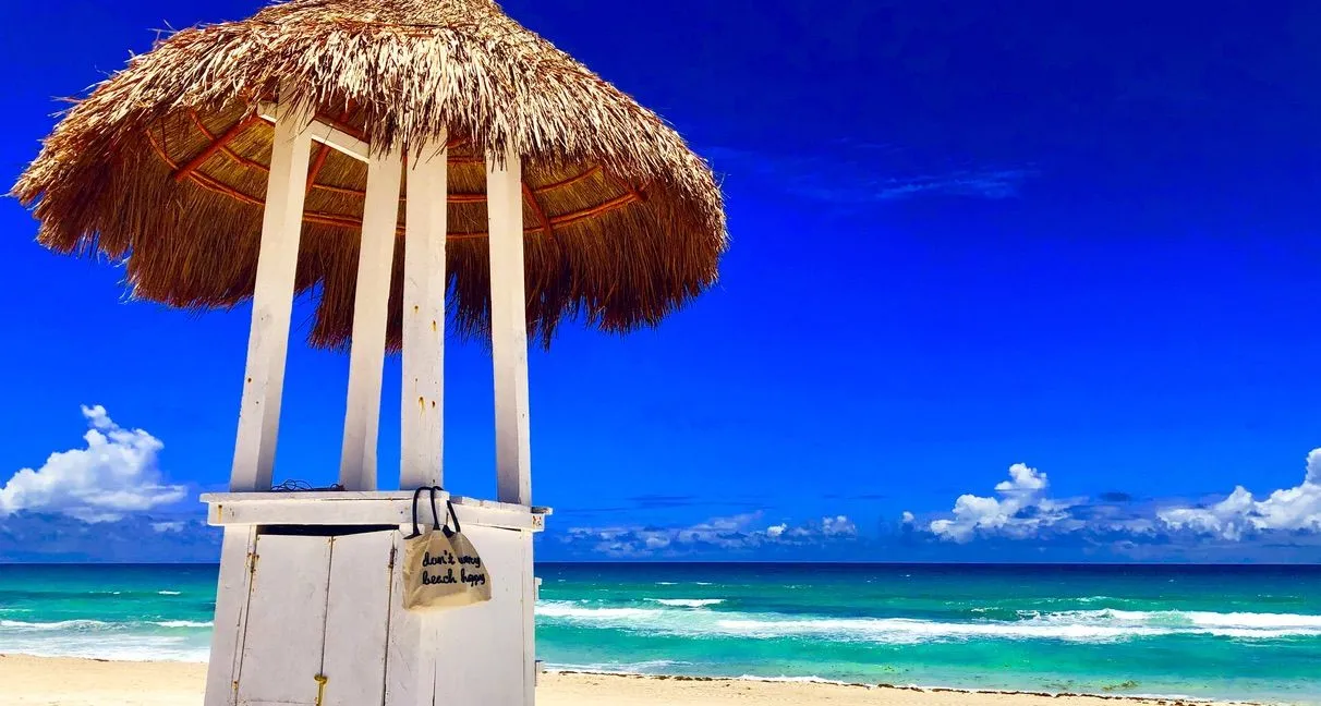 Thatched-roof beach hut on white sand with turquoise Caribbean Sea and blue sky behind it